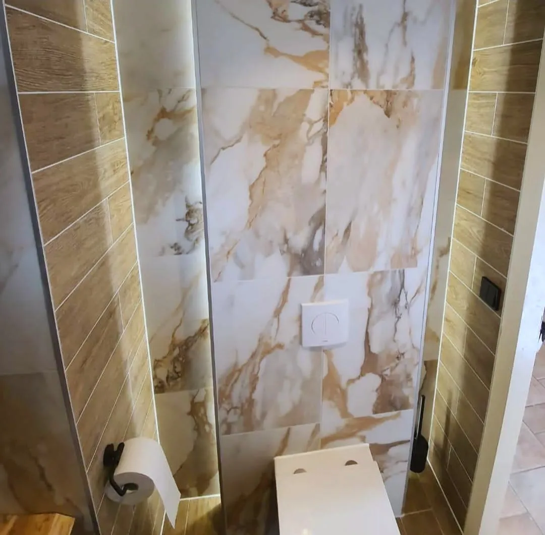 Toiletruimte met marmerlook tegels met warme adering, verlichte voegen langs de wanden en een zwevend toilet