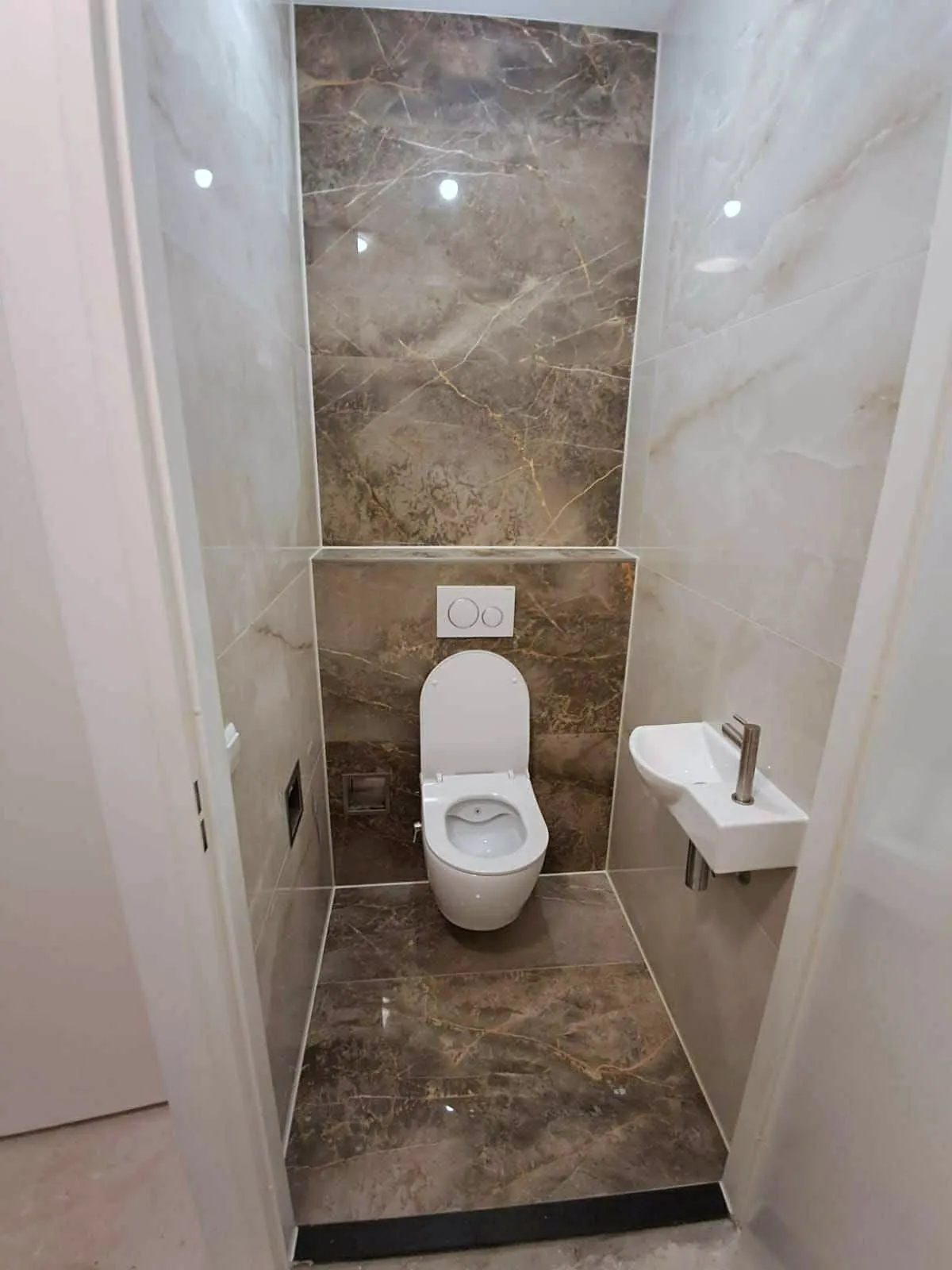 Toilet met natuursteenlook wandtegels, een zwevende pot en een kleine fontein