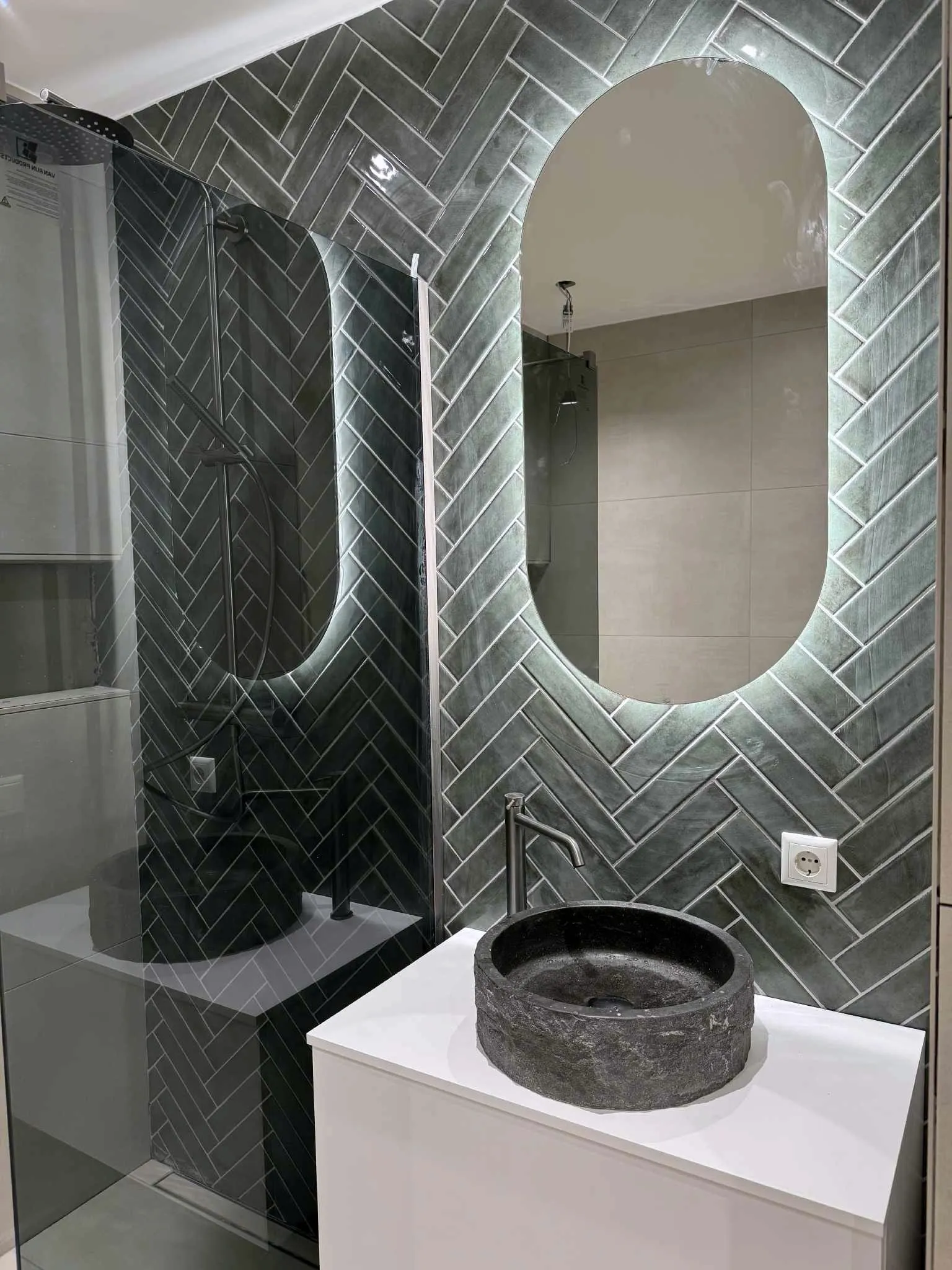 Badkamer met groene visgraattegels, een ovale spiegel met verlichting en een wastafelkom van natuursteen