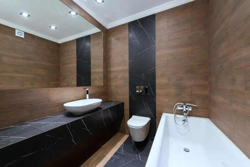 Badkamer met zwart marmer, een houten wand, een zwevend toilet en een ligbad